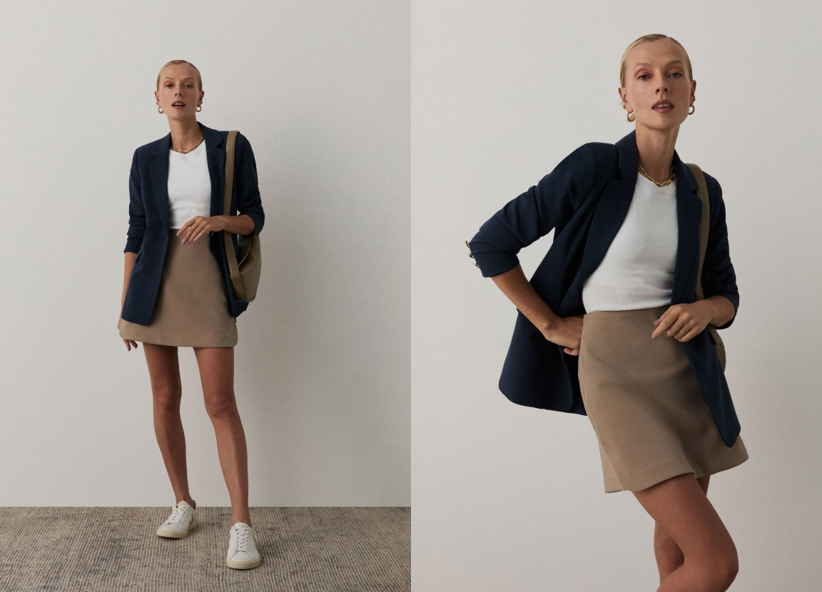 modelo posando com saia bege, camisa branca e blazer azul com tênis representando looks de trabalho no verão