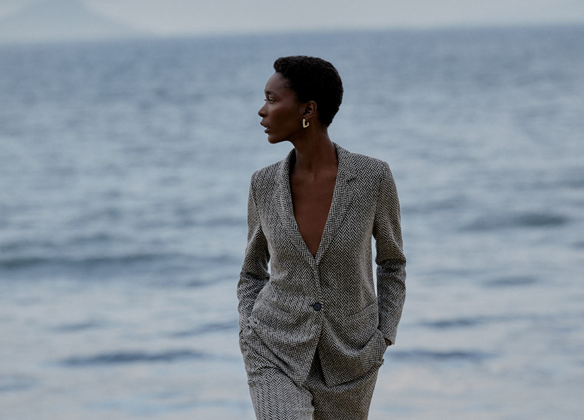 mulher com conjunto de alfaiataria em frente ao mar representando as tendências para o inverno