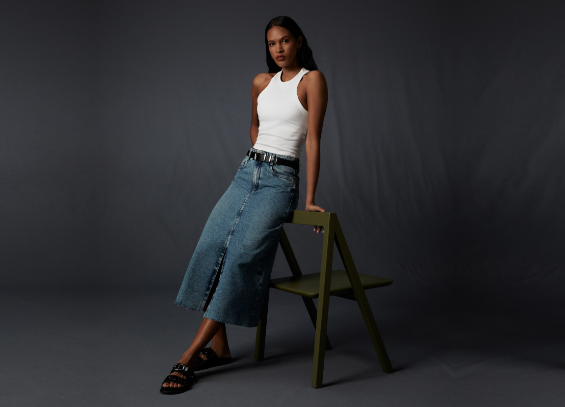 modelo com regata branca e saia jeans com fenda representando o que não pode faltar no guarda-roupa