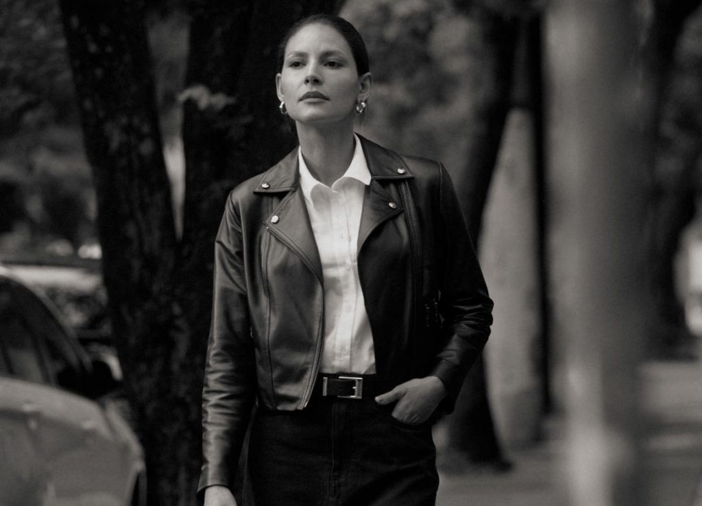 Mulher usando jaqueta de couro preta, camisa branca e calça preta com cinto.