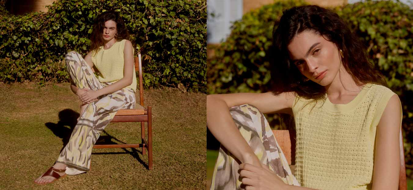 Modelo usando look em tons pasteis, sentada em cadeira ao ar livre.